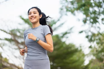 Deurstickers Happy slim woman wearing sportswear jogging in the city at sunrise. Young beautiful asian female in sports bra running outdoor. Workout exercise in the morning. Healthy and active lifestyle concept. © Chanakon
