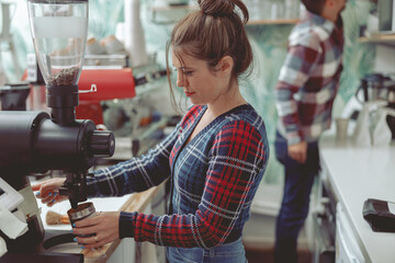 Woman barista working in coffee shop near coffee grinder