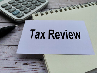 Tax review text on small white card with notepad, pen and calculator background. Tax concept.