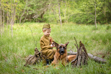 a boy in a military uniform in a clearing, sitting by a campfire with a German shepherd.Two friends...