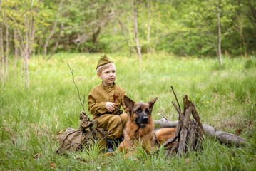 a boy in a military uniform in a clearing, sitting by a campfire with a German shepherd.Two friends...
