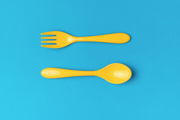A set of yellow plastic spoon and fork on a blue background. Flat lay.