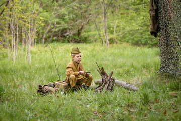 a small child in a beautiful military victory uniform, playing in nature and eating soldier porridge