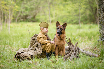 a boy in a military uniform in a clearing, sitting by a campfire with a German shepherd.Two friends...