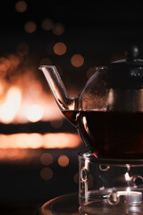 partial view of a glass pot with dark tea on a glass warmer with a candle on a table in front of...