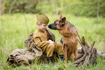 a boy in a military uniform in a clearing, sitting by a campfire with a German shepherd.Two friends...