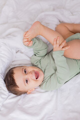 Obraz na płótnie Canvas cute smiling baby in a green cotton bodysuit is lying on a white bed on his back. top view