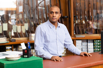 Portrait of confident owner of an arms shop in front of a shop window with hunting rifles