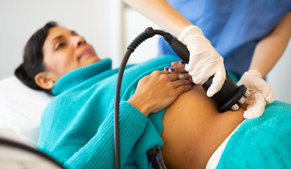 Close up view of young adult woman belly receiving radio frequency abdomen lifting procedure at cosmetology clinic