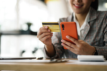 Online payment, happy Asian woman hands holding a credit card and using smart phone for online...