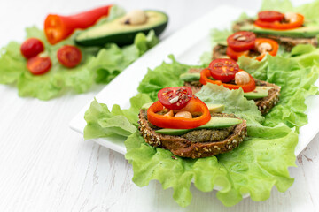 Sandwiches with rye bread, tomatoes, avocados, peppers and spicy sauce on a white plate covered with lettuce. Diet breakfast. healthy eating. Vegan snack Side view, close-up