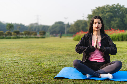 Young indian girl doing yoga wearing yoga pants in the park. Girls working out early in the morning. Healthy lifestyle concept.