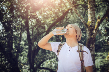Young attractive male with hat drinking water from plastic fitness bottle after walking forest. Sport,  youth wellbeing.