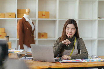 Asian woman designer are thinking and drawing something on paper for customers order items at the designer desk in the studio. Clothes designers are working in the office. Startup designer concept.
