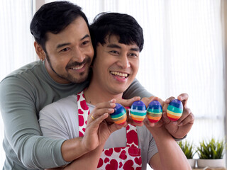 Happy Asian LGBT gay couple showing diy colorful stripes Easter eggs with happiness. LGBTQ lifestyle Easter Holidays.
