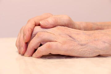 Wrinkled grandmother's hands folded, on a white background