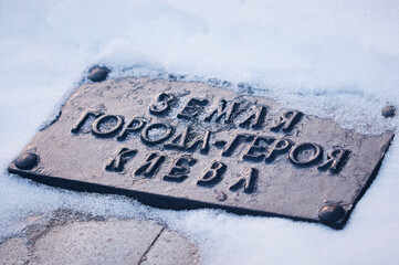 The inscription in Russian: the land of the city of the hero of Kyiv. A fragment of the monument to the fallen heroes of World War II. Morning after snowfall.