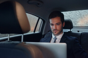 Get working done during his commute. Shot of a businessman sitting in the backseat of a car working on a laptop.