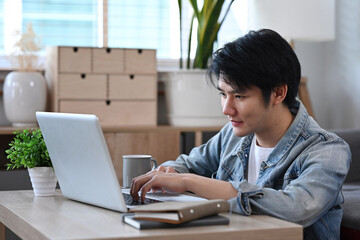Fototapeta premium Asian male freelancer sitting on floor in living room and working online with laptop.