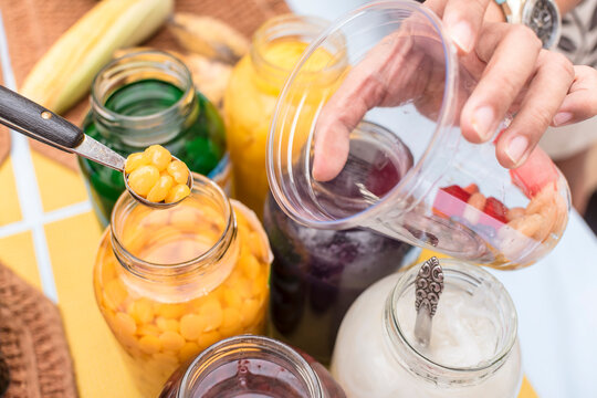 Adding yellow kaong into a clear plastic cup. Making Halo-halo, a FIlipino dessert.