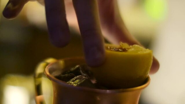 Fingers moving cut lemon onto ice cold tropical style beverage inside copper cup filmed in extreme close up and slow motion