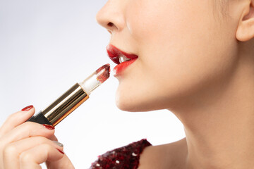 Close up profile view of young beautiful woman with red lips holding her Mutelu lipstick. Photo...