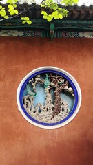 a hollowed out art window in a ancient wall with green leaves and landscape paintings on the wall eaves