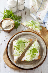 Healthy breakfast or holiday snacks. Toast with cucumbers, herbs and ricotta on a rustic wooden table.