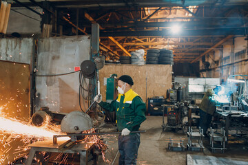 Workers working with metal construction on plant. Metal processing with big angle grinder disk saw and welder welding. Sparks in metalworking at factory.