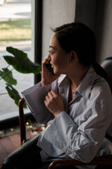 Attractive smiling young asian woman relaxing in cafe, working on laptop computer, talking on mobile phone