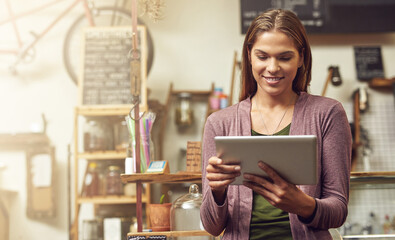 Fototapeta premium Keeping a record of her business goals on her tablet. Shot of a young entrepreneur using a digital tablet in her store.