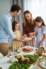 Vertical image of cheerful caucasian family of four sharing with egg during easter dinner