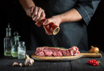 Professional chef prepares raw veal meat. Before baking, the chef adds pepper to the beef. National dish is being prepared in the kitchen