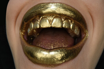 Gold lips. Gold paint from the mouth. Golden lips on woman mouth with make-up.