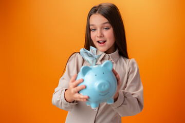 Teen girl with piggy bank on orange color background.