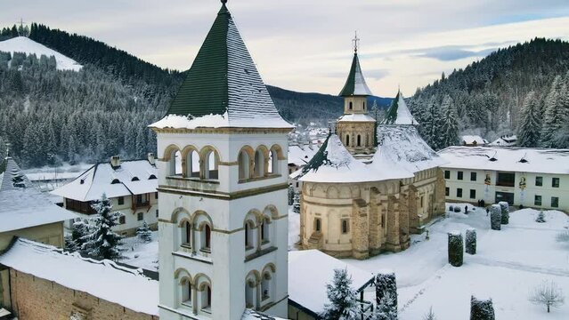 Aerial drone view of Putna Monastery in winter, Romania. Inner yard with walking tourists, bare trees, snow, hills around