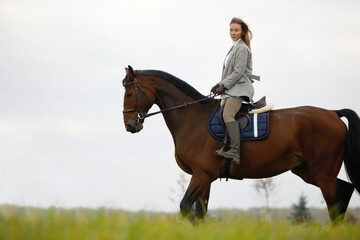 Beautiful young woman riding a horse on the field. Sideways to the camera. Freedom, joy, movement