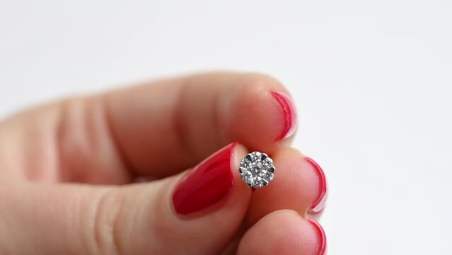 Close view of a woman holding earring with diamonds. White background, hands with red nails