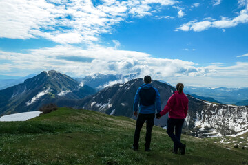 Fototapeta na wymiar Active couple hiking on Frauenkogel with scenic view on mountain peaks in the Karawanks, Carinthia, Austria. Border with Slovenia. Triglav National Park. Kahlkogel (Golica). Snow melting in spring