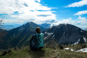Naklejka premium Female hiker having a break in spring on the summit of Frauenkogel in the Karawanks in Carinthia, Austria, Europe. Borders with Slovenia. Triglav National Park. Looking on Kahlkogel and Hahnkogel.