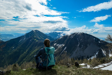 Naklejka premium Female hiker having a break in spring on the summit of Frauenkogel in the Karawanks in Carinthia, Austria, Europe. Borders with Slovenia. Triglav National Park. Looking on Kahlkogel and Hahnkogel.