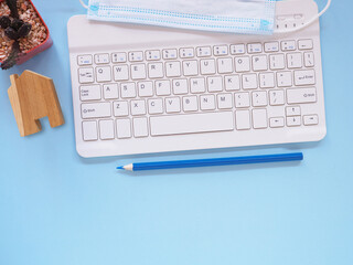 Flat lay, blue office desktop with key board, medical face mask and cactus. Top view with space for text. Business, education and work from home concept.