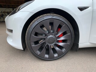 Detailed and cleaned car wheel with black matte rim. White car with black rims and red brake callipers.