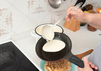 Senior woman chef pour portion of liquid dough by hands with ladle on frying pan for baking delicious pancakes, crepes in the kitchen in the morning for tasty breakfast. Selective focus. Maslenitsa. 