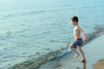 Happy child boy joyfully runs to swim in the sea. Summer and travel concept