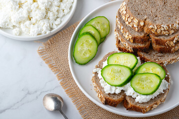Slices of rye bread with cottage cheese and cucumbers on white background