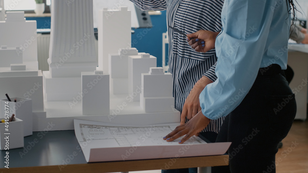 Poster close up of architects placing blueprints plan on table to work on urban project with building model