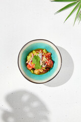 Vegetables salad with tomatoes, cucumbers and onion on white table with hard shadow. Vegan starter in asian style. Summer menu concept. Asian food in minimal design with sun light shadow.