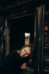 beautiful Ukrainian girl in black clothes near the old wooden house. The war in Ukraine. Portrait of a woman on a dark wooden background. Old abandoned wooden house. Old wooden window frame