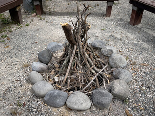 Unlit wooden kindling and sticks stacked together within a ring of stones forming a small camping...